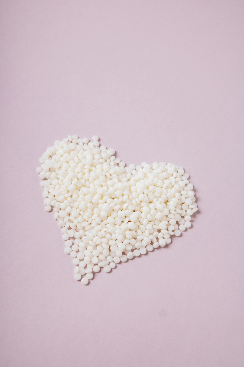 Hard wax beads in a heart shape on a soft pink background